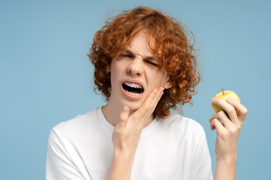 Foods to Avoid with Braces – Keep Your Smile Safe. A boy is experiencing discomfort and holding an apple in his hand